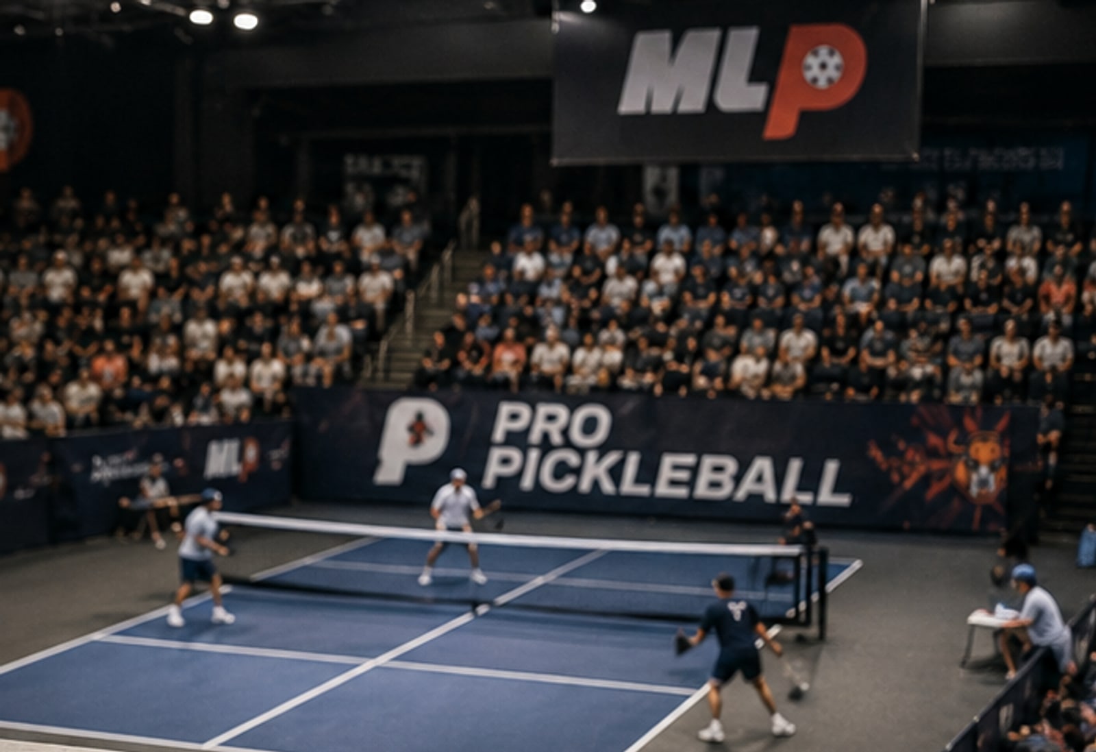 A Major League Pickleball doubles match in progress, viewed from a stadium seat — packed stands rising behind the court, MLP and Pro Pickleball signage on the boards, four players at the kitchen line. The picture an aspiring host city is trying to put itself in.